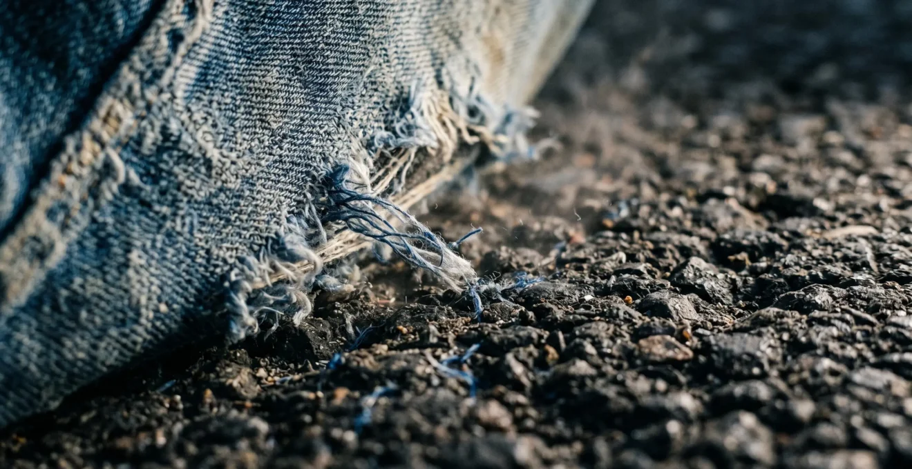 Détail macro d'un textile de jean classique en contact avec une surface rugueuse illustrant le danger de l'abrasion sur asphalte
