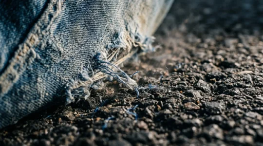 Détail macro d'un textile de jean classique en contact avec une surface rugueuse illustrant le danger de l'abrasion sur asphalte