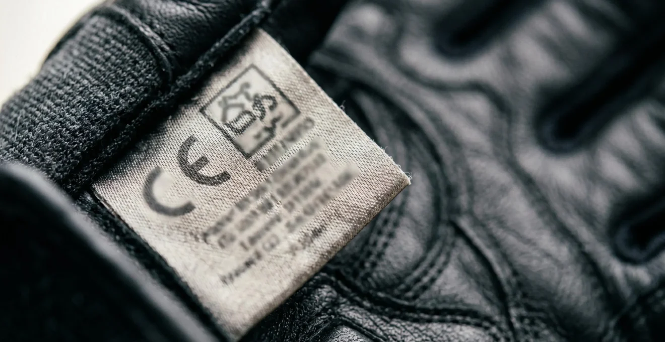 Gros plan sur l'étiquette CE EPI à l'intérieur d'un gant de moto noir, avec le pictogramme motard et la norme EN 13594 visible
