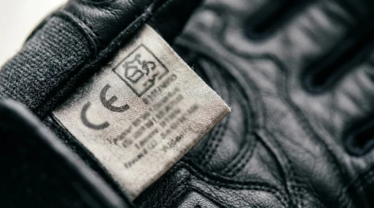 Gros plan sur l'étiquette CE EPI à l'intérieur d'un gant de moto noir, avec le pictogramme motard et la norme EN 13594 visible